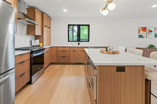 kitchen with a breakfast bar, wall chimney range hood, light countertops, light wood finished floors, and stainless steel appliances