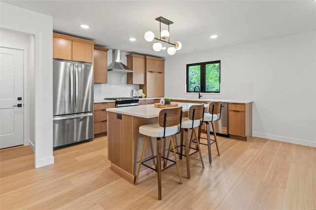 kitchen featuring wall chimney range hood, a kitchen breakfast bar, a kitchen island, appliances with stainless steel finishes, and light wood-style flooring