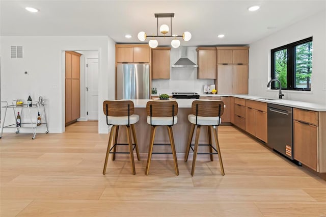 kitchen featuring a kitchen bar, wall chimney exhaust hood, a sink, light wood finished floors, and stainless steel appliances
