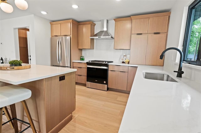 kitchen featuring wall chimney range hood, a sink, light brown cabinets, a breakfast bar, and stainless steel appliances
