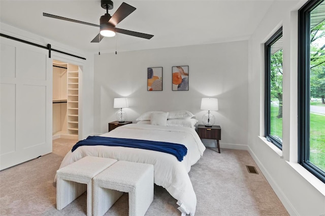 bedroom featuring a barn door, visible vents, light carpet, and a walk in closet