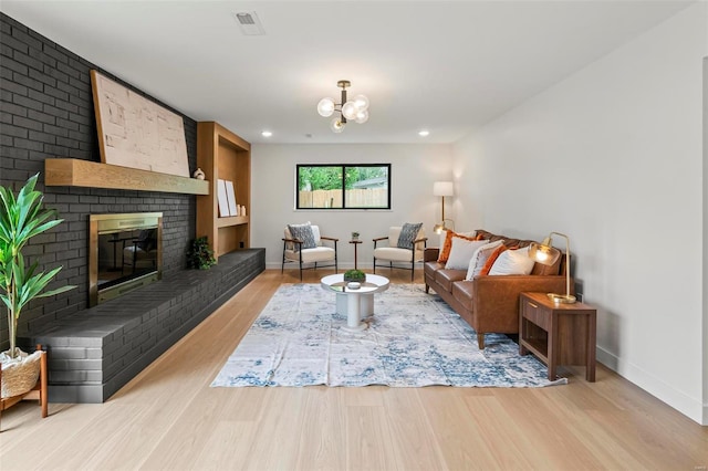 living area with visible vents, a fireplace, baseboards, light wood-type flooring, and a notable chandelier