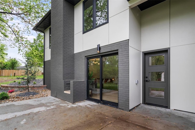 view of exterior entry with fence, a patio area, and brick siding