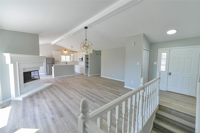 unfurnished living room featuring baseboards, light wood-type flooring, and vaulted ceiling with beams