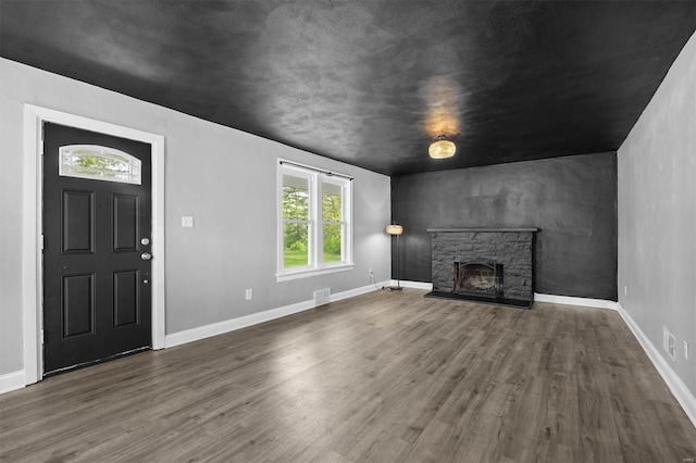 unfurnished living room with visible vents, baseboards, wood finished floors, and a stone fireplace