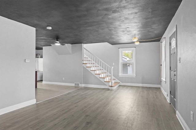 unfurnished living room with stairway, baseboards, wood finished floors, and visible vents