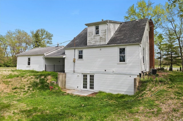 back of property featuring central AC, roof with shingles, french doors, a chimney, and a yard
