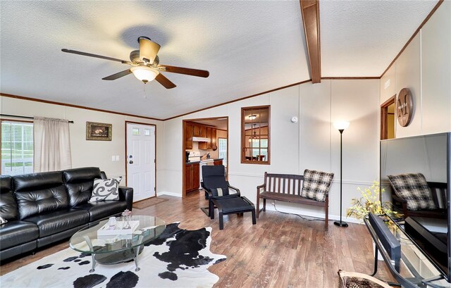 living room with ceiling fan, a textured ceiling, wood finished floors, vaulted ceiling with beams, and ornamental molding