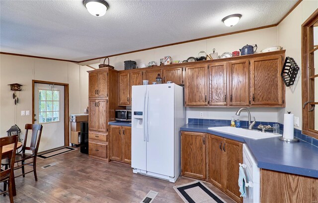 kitchen featuring brown cabinetry, a textured ceiling, stainless steel microwave, a sink, and white fridge with ice dispenser