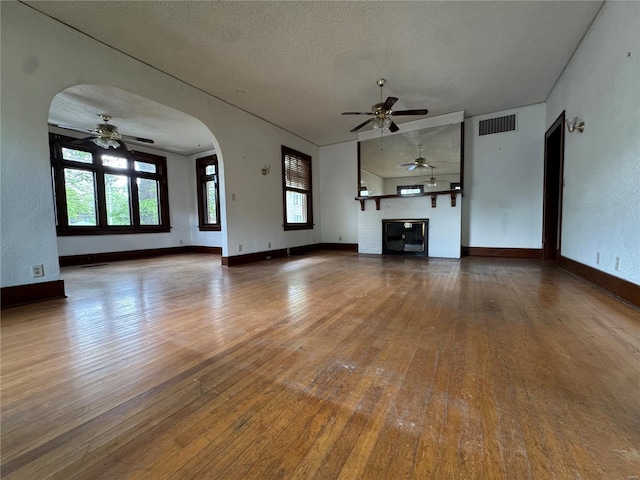 unfurnished living room featuring wood-type flooring, ceiling fan, visible vents, and a wealth of natural light