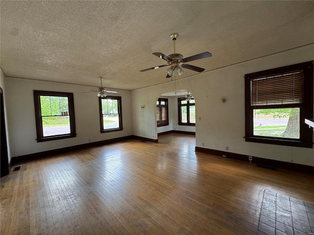 unfurnished room featuring a ceiling fan, a textured ceiling, arched walkways, and hardwood / wood-style floors