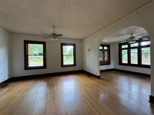 empty room featuring wood-type flooring, a ceiling fan, arched walkways, and visible vents