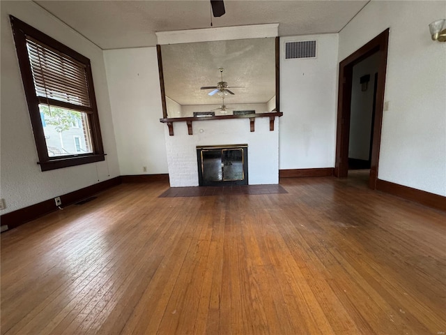 unfurnished living room with a large fireplace, a ceiling fan, hardwood / wood-style floors, and visible vents