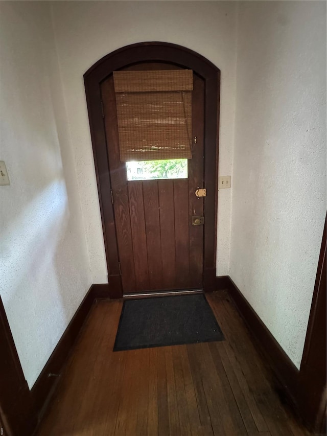 doorway to outside with arched walkways, baseboards, and dark wood-type flooring