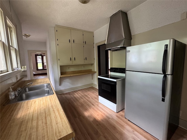 kitchen featuring wall chimney range hood, a sink, electric range oven, freestanding refrigerator, and light wood-type flooring