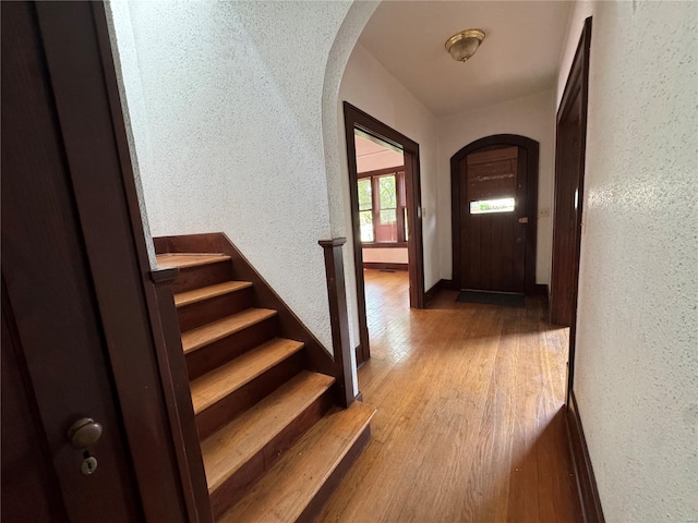 doorway featuring arched walkways, a textured wall, and wood finished floors