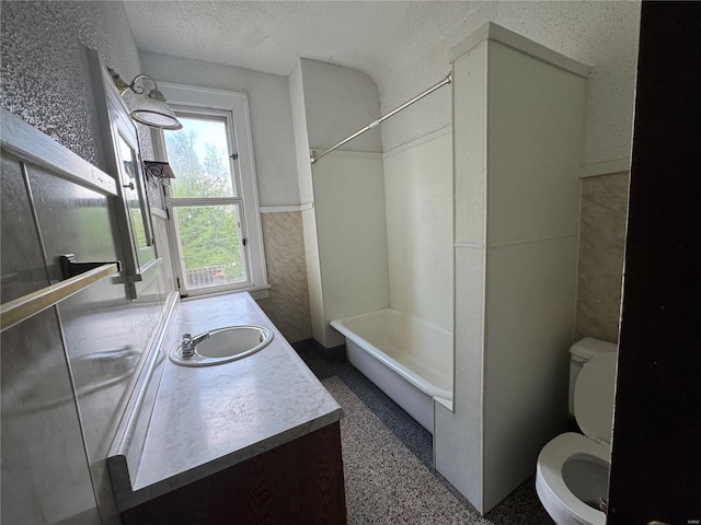 full bathroom with vanity, toilet, a textured ceiling, a wainscoted wall, and  shower combination