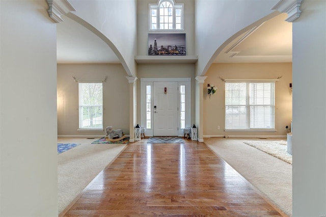 carpeted entrance foyer with baseboards, arched walkways, a high ceiling, and wood finished floors