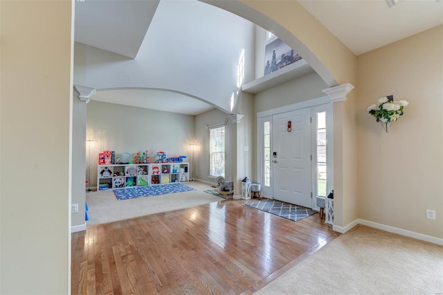 foyer entrance with a towering ceiling, arched walkways, wood finished floors, baseboards, and carpet