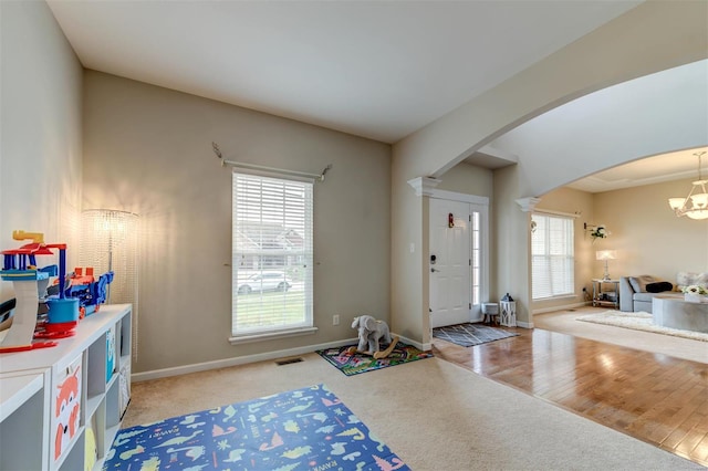 entryway with an inviting chandelier, visible vents, light carpet, baseboards, and arched walkways