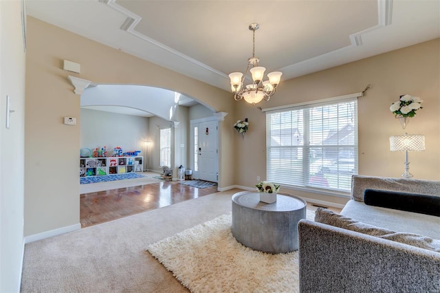 living area with a notable chandelier, a raised ceiling, arched walkways, carpet, and baseboards