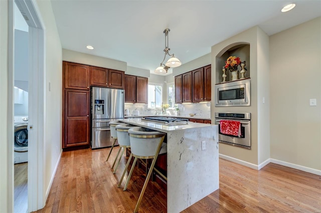 kitchen featuring a center island, stainless steel appliances, washer / dryer, light wood-type flooring, and pendant lighting