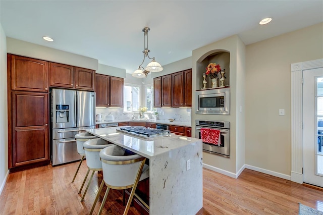 kitchen with light wood-style flooring, stainless steel appliances, decorative light fixtures, decorative backsplash, and a kitchen island