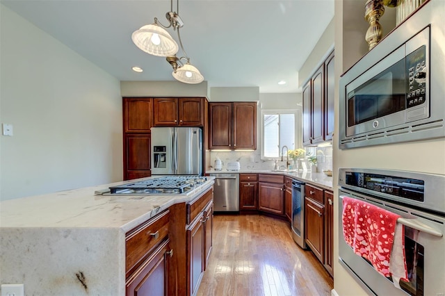 kitchen featuring light stone countertops, appliances with stainless steel finishes, light wood-style flooring, a kitchen island, and pendant lighting