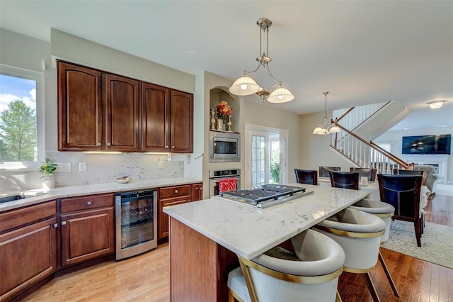 kitchen with wine cooler, a breakfast bar area, light stone counters, light wood finished floors, and appliances with stainless steel finishes