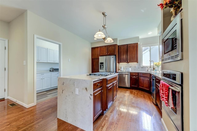 kitchen with appliances with stainless steel finishes, light stone countertops, light wood-style flooring, and visible vents