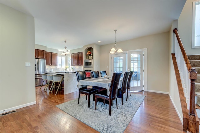 dining area with visible vents, light wood finished floors, stairs, and a notable chandelier