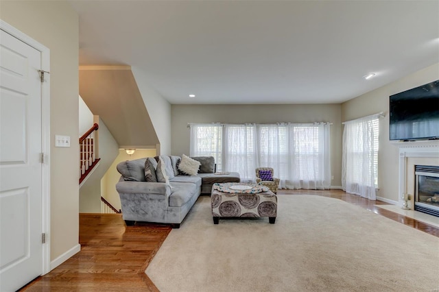 living room featuring a fireplace with flush hearth, wood finished floors, stairway, baseboards, and recessed lighting