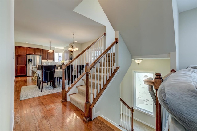 stairs with baseboards, wood finished floors, and a chandelier