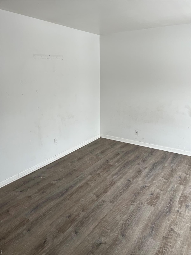 spare room featuring baseboards and dark wood-style floors