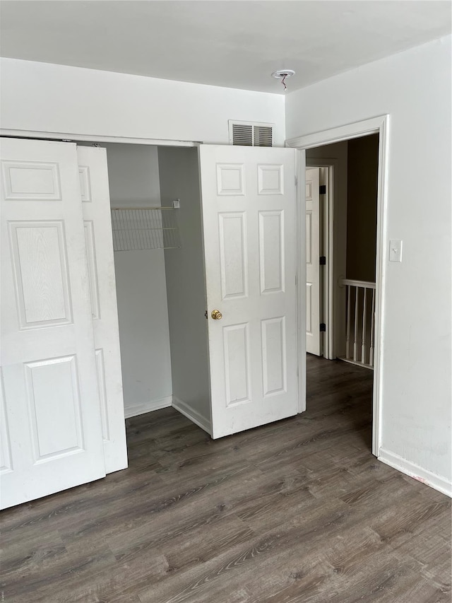 unfurnished bedroom with baseboards, a closet, dark wood-style flooring, and visible vents