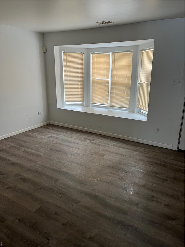 unfurnished room featuring baseboards, dark wood finished floors, and visible vents