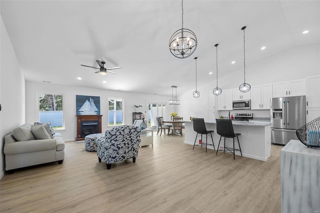 living area with a fireplace, high vaulted ceiling, ceiling fan with notable chandelier, light wood-style floors, and recessed lighting