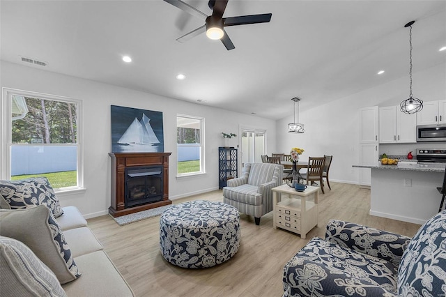 living area featuring ceiling fan, visible vents, vaulted ceiling, baseboards, and light wood-style flooring