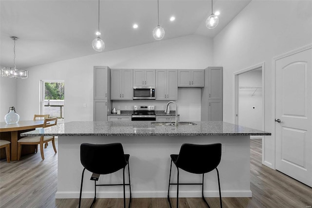 kitchen featuring a sink, high vaulted ceiling, gray cabinets, stainless steel appliances, and a kitchen bar