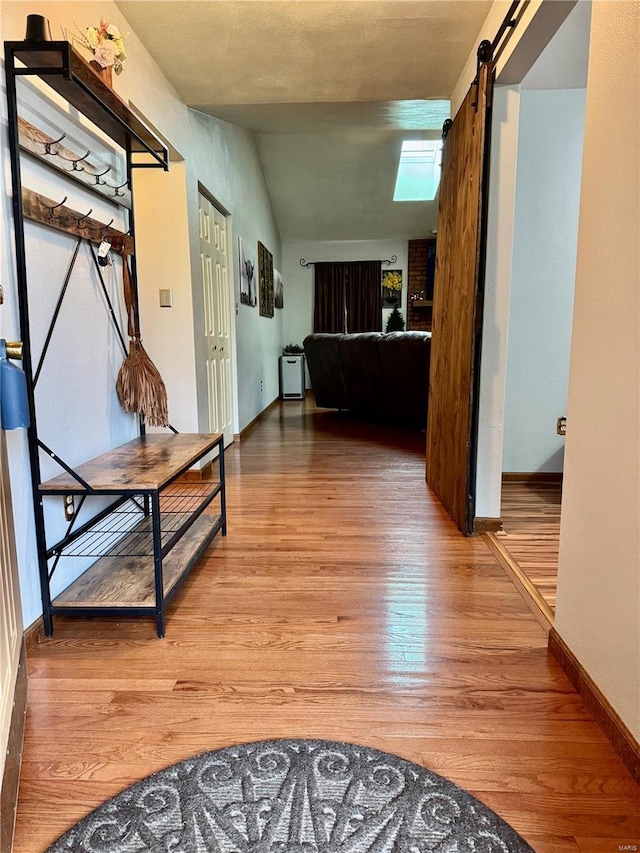 hallway with baseboards, vaulted ceiling, light wood finished floors, and a barn door
