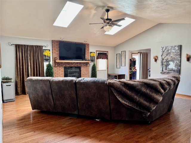 living room with ceiling fan, wood finished floors, vaulted ceiling with skylight, and a fireplace