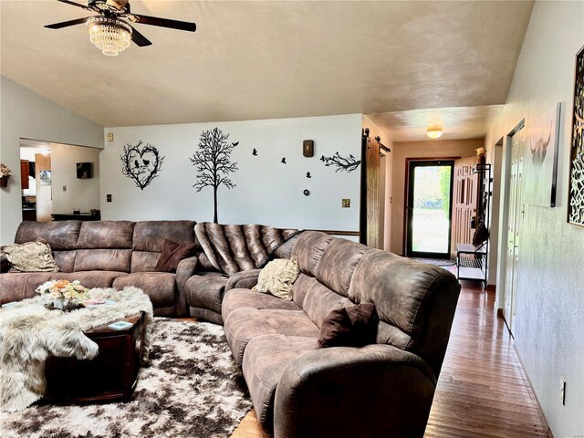 living room with a ceiling fan, a barn door, and wood finished floors