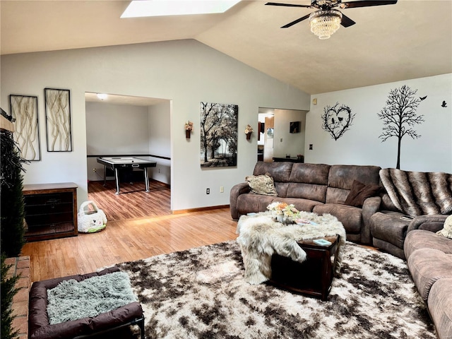 living area featuring baseboards, ceiling fan, wood finished floors, and vaulted ceiling with skylight