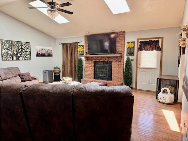 living area featuring a brick fireplace, wood finished floors, baseboards, lofted ceiling with skylight, and ceiling fan