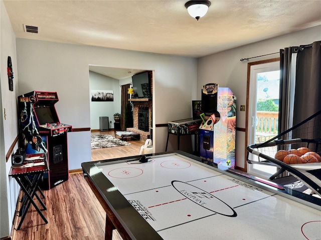 game room featuring visible vents, baseboards, a brick fireplace, and wood finished floors