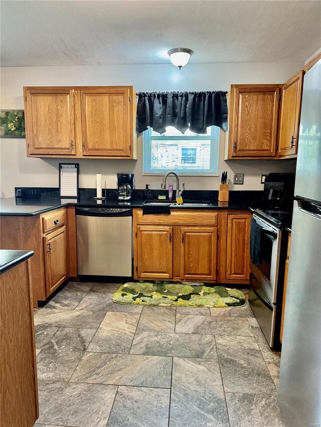 kitchen with brown cabinets, stainless steel appliances, stone finish floor, and a sink
