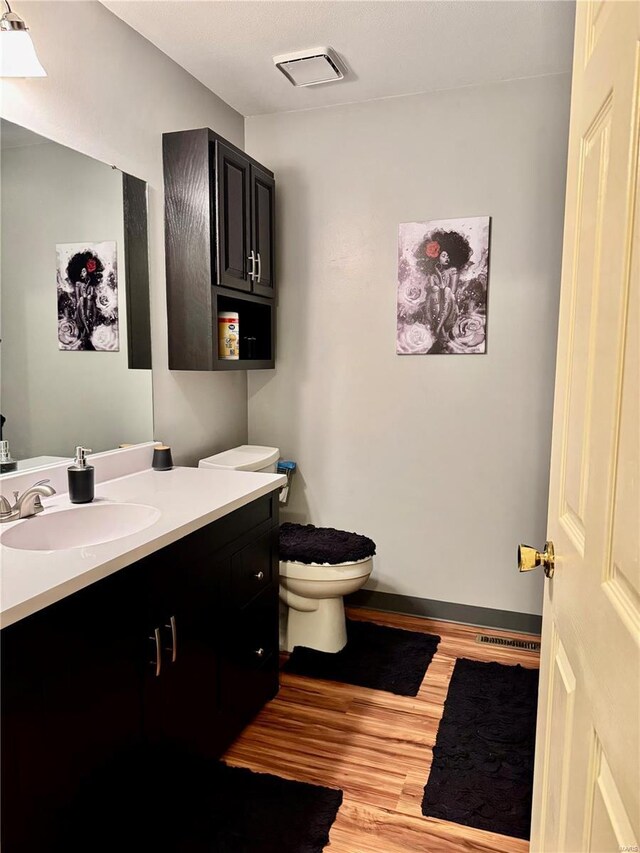 half bath featuring visible vents, wood finished floors, vanity, baseboards, and toilet