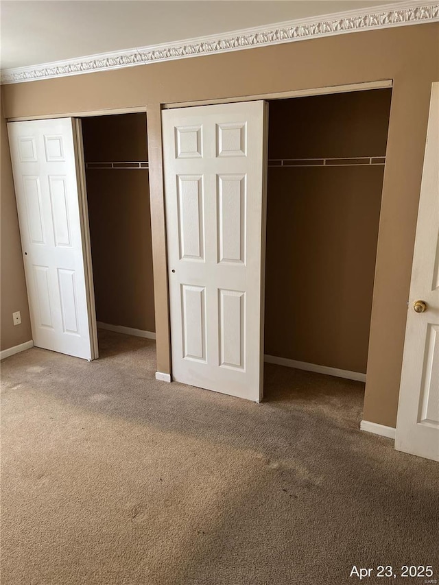 unfurnished bedroom with carpet floors, baseboards, and two closets