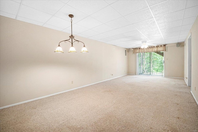 carpeted empty room featuring baseboards, a drop ceiling, and a notable chandelier