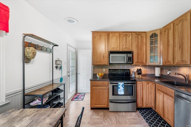 kitchen featuring dark countertops, tasteful backsplash, a sink, glass insert cabinets, and stainless steel appliances